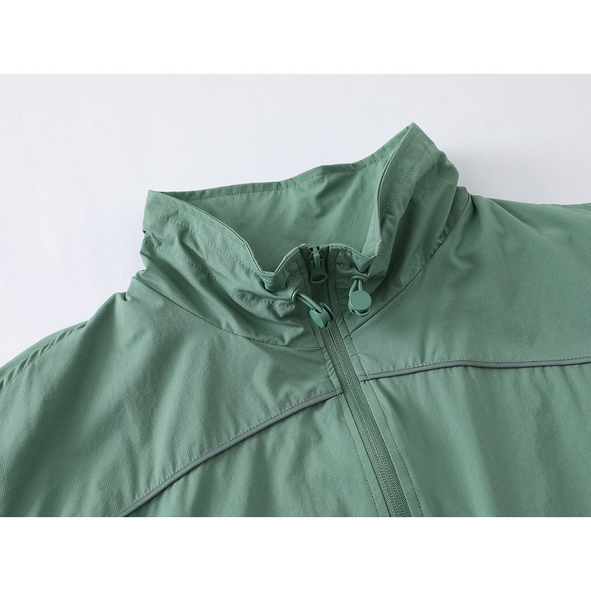 Close-up of a sage-green jacket’s high collar, center zipper, and curved piping.