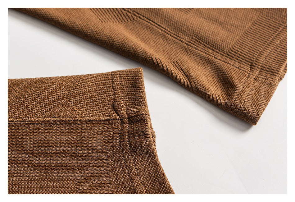 Close-up of a warm brown knit garment showing textured stitches and a seam near the edge.