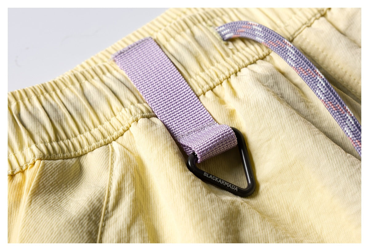 Close-up of pale yellow shorts showing the elastic waistband, lavender webbing loop, and drawcord.