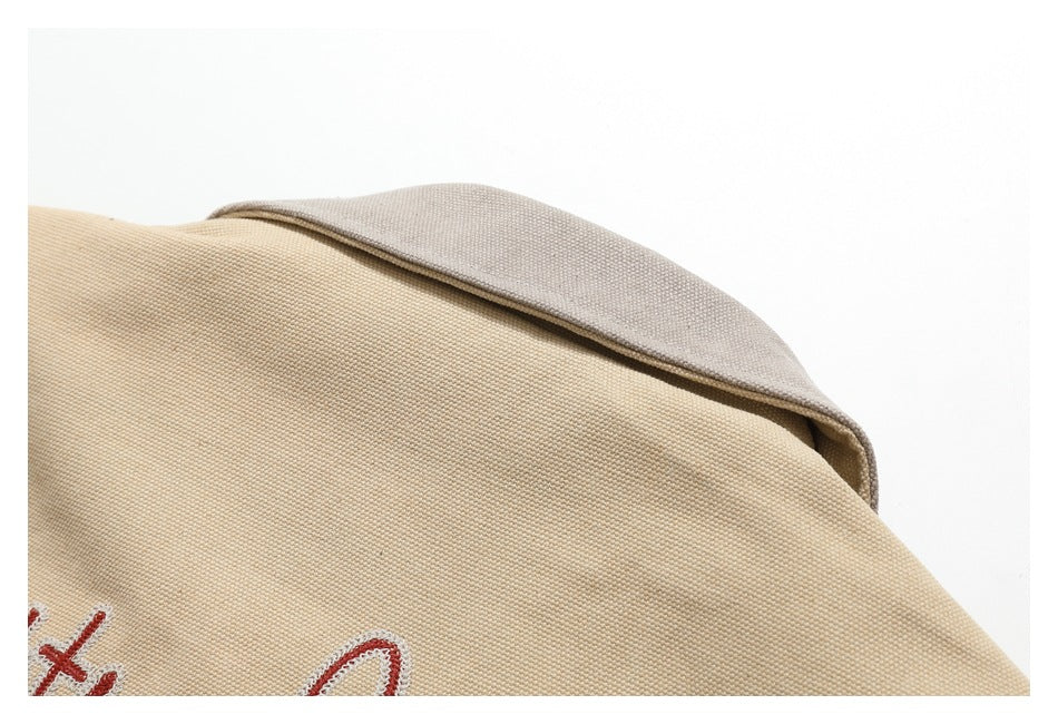 Close-up of a beige textured garment with a contrasting gray-beige collar and partial red embroidery.