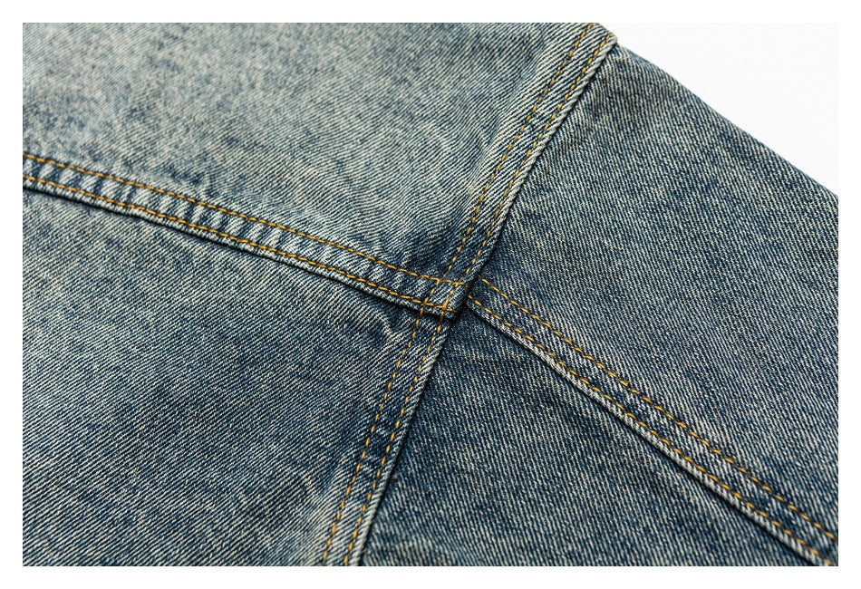 Close-up of intersecting seams and golden stitching on faded blue denim.