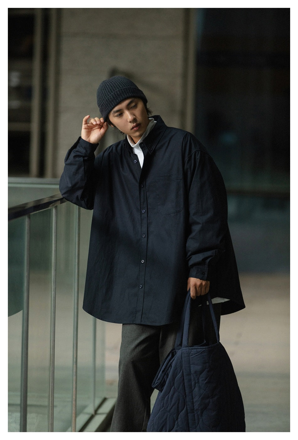 Closer front view of a model wearing an oversized black button-front shirt with a chest pocket and black beanie.