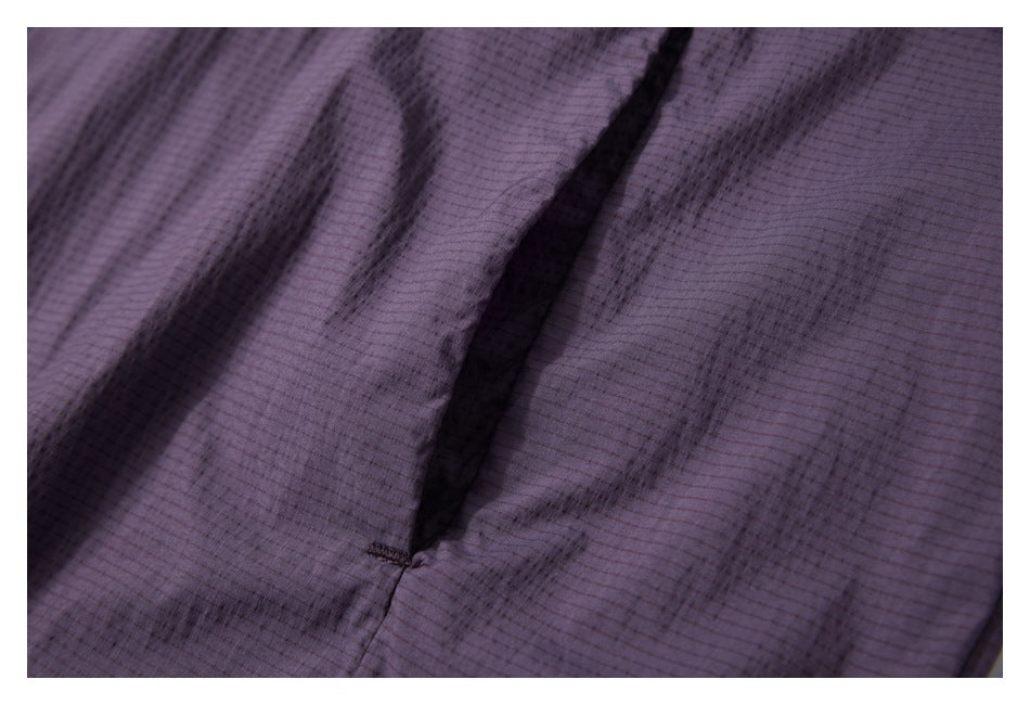 Close-up of dark purple jacket fabric showing a narrow seam opening and fine grid texture.