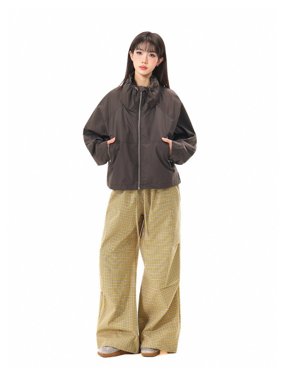 Model wearing a dark brown zip-front jacket with a gathered high collar and yellow checked trousers, front view.