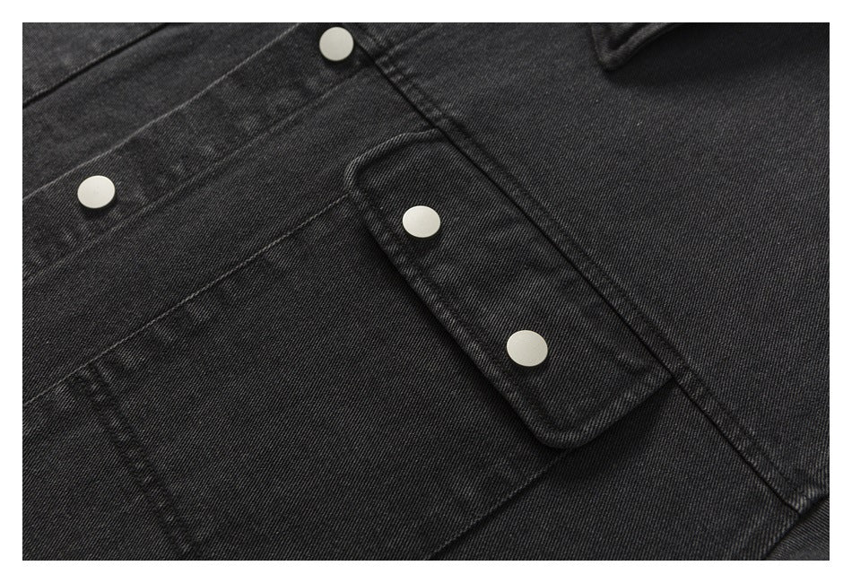 Close-up of a black denim jacket chest pocket flap and silver snap buttons.