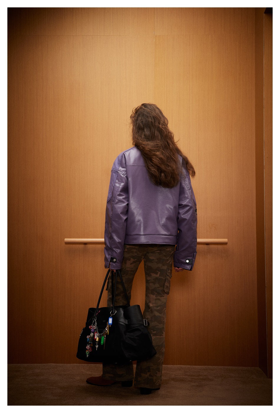 Back view of a model wearing a plain purple jacket and camouflage pants, carrying a black bag.