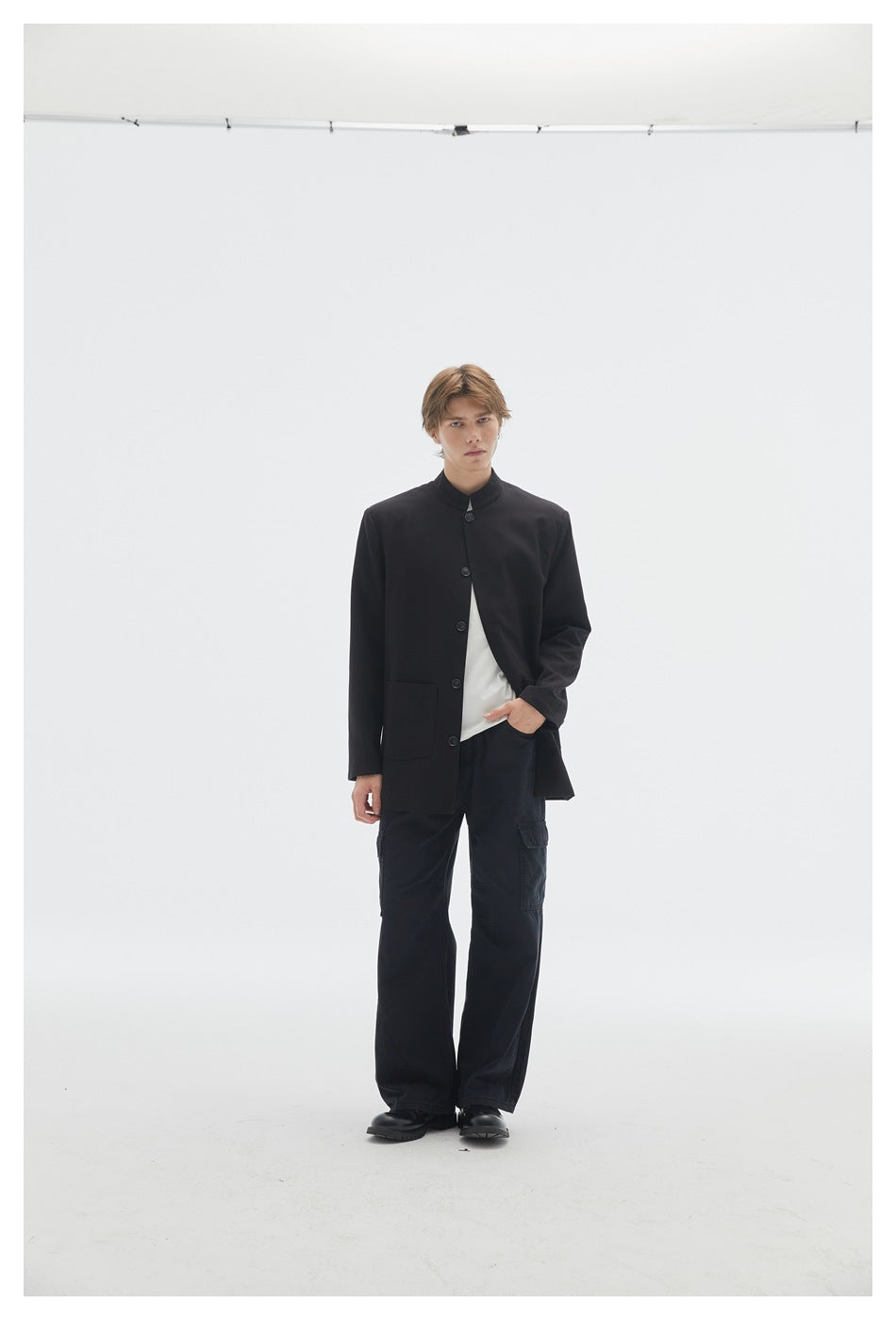 Front view of a model in a black stand-collar button-front jacket, white T-shirt and black cargo trousers.