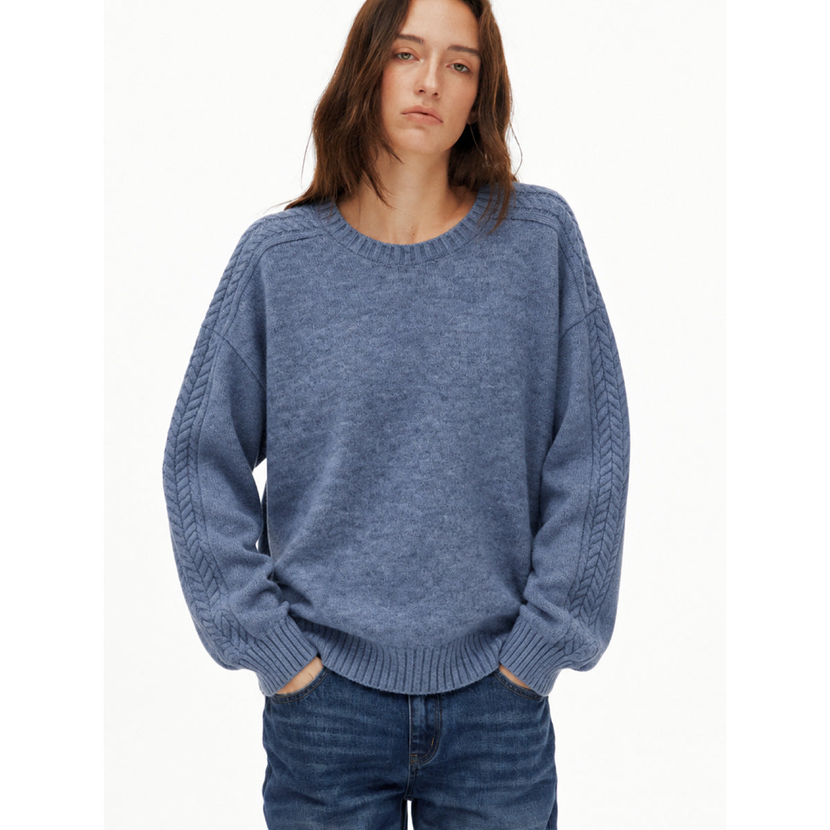 Close view of a model wearing a blue-gray crewneck sweater with cable-knit detailing along the sleeves.