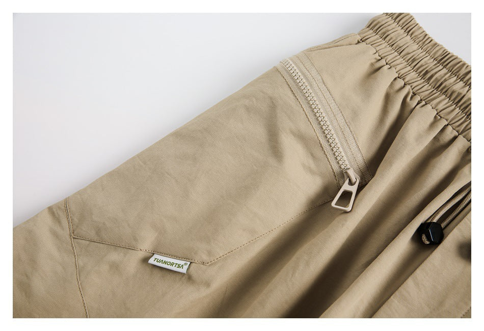Close-up of beige pants showing a zippered pocket, elastic waistband, stitching, and a small sewn label.