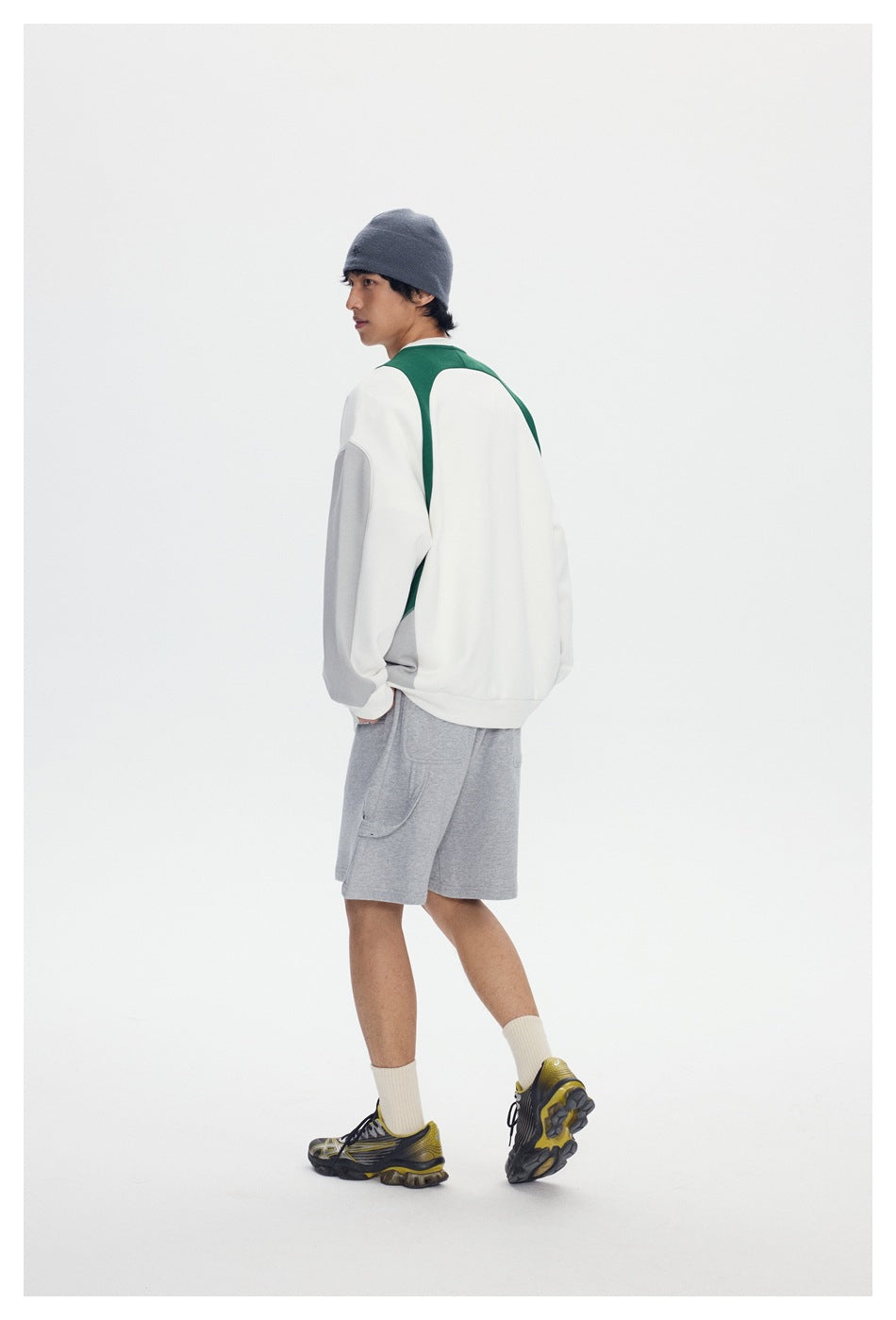 Back view of a model wearing a white sweatshirt with green and gray panels and gray shorts.