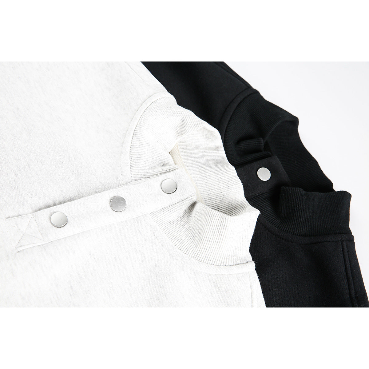 Close-up of light gray and black stand-collar sweatshirts with snap-button plackets.