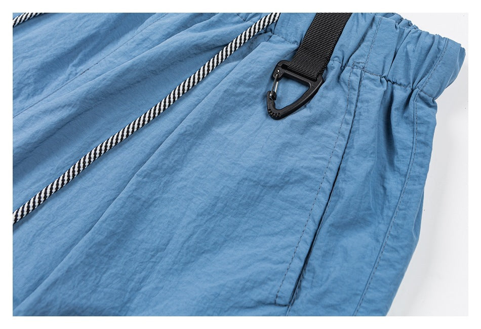 Close-up of blue shorts showing the elastic waistband, striped drawstring, black clip, and side pocket seam.