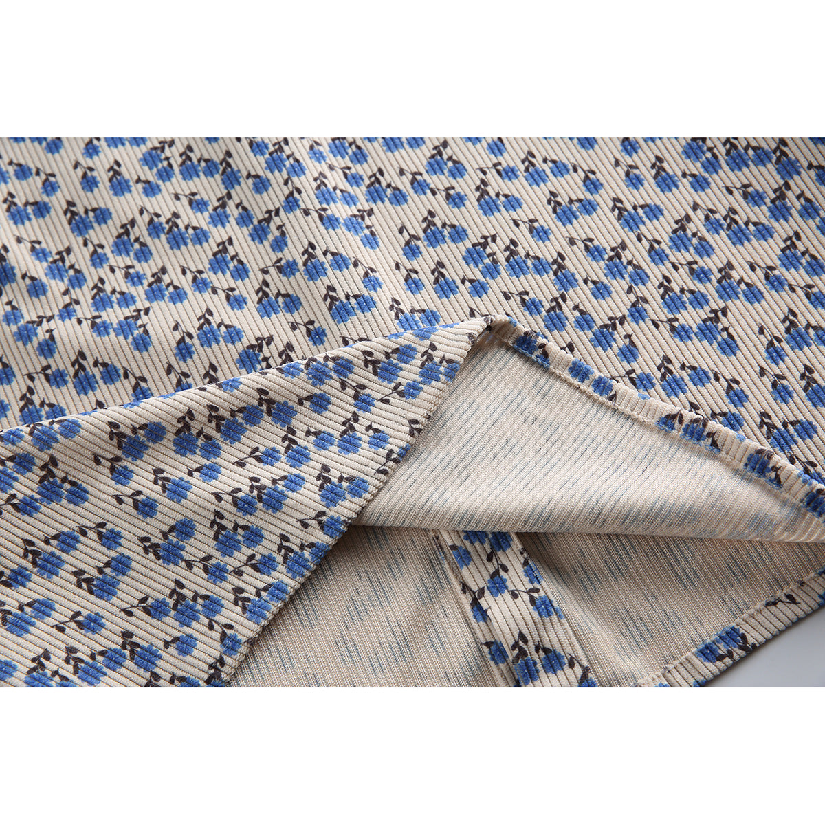 Close-up of the beige shirt's blue floral ribbed fabric with a folded hem showing the reverse and stitching.