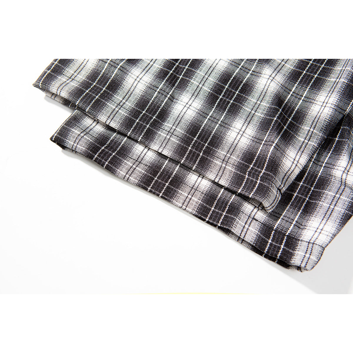Close-up of folded black, gray, and white plaid shirt fabric showing its pattern and stitched edge.