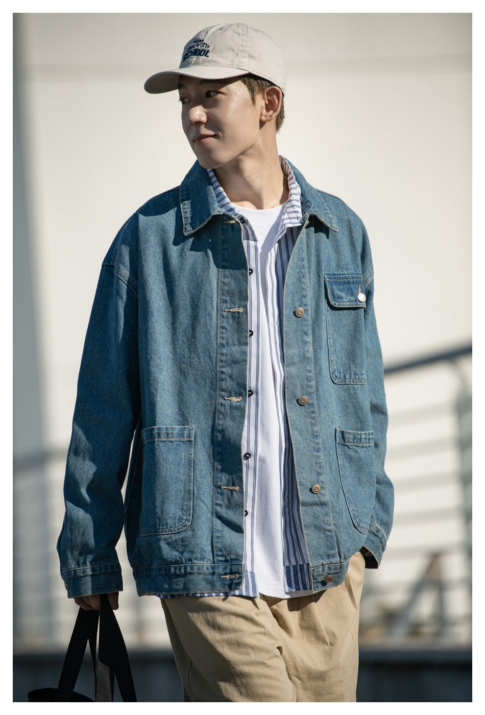 Model wearing a blue denim jacket over a blue-and-white striped shirt and white tee, with tan trousers and a cap.