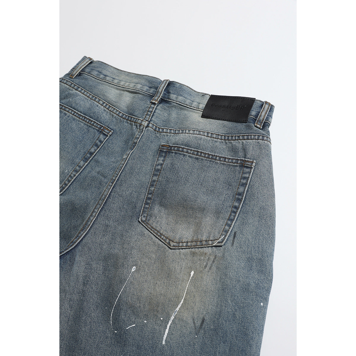 Partial back view of faded blue jeans with a rear pocket, belt loops and white paint streaks.