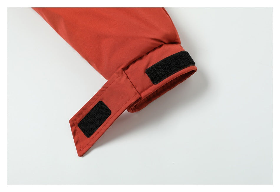 Close-up of a rust-red jacket sleeve cuff with two black hook-and-loop adjustment tabs.