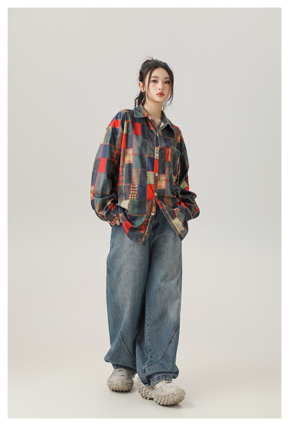 Model wearing a loose patchwork shirt with red, navy, green and tan blocks, wide-leg jeans and chunky sneakers.