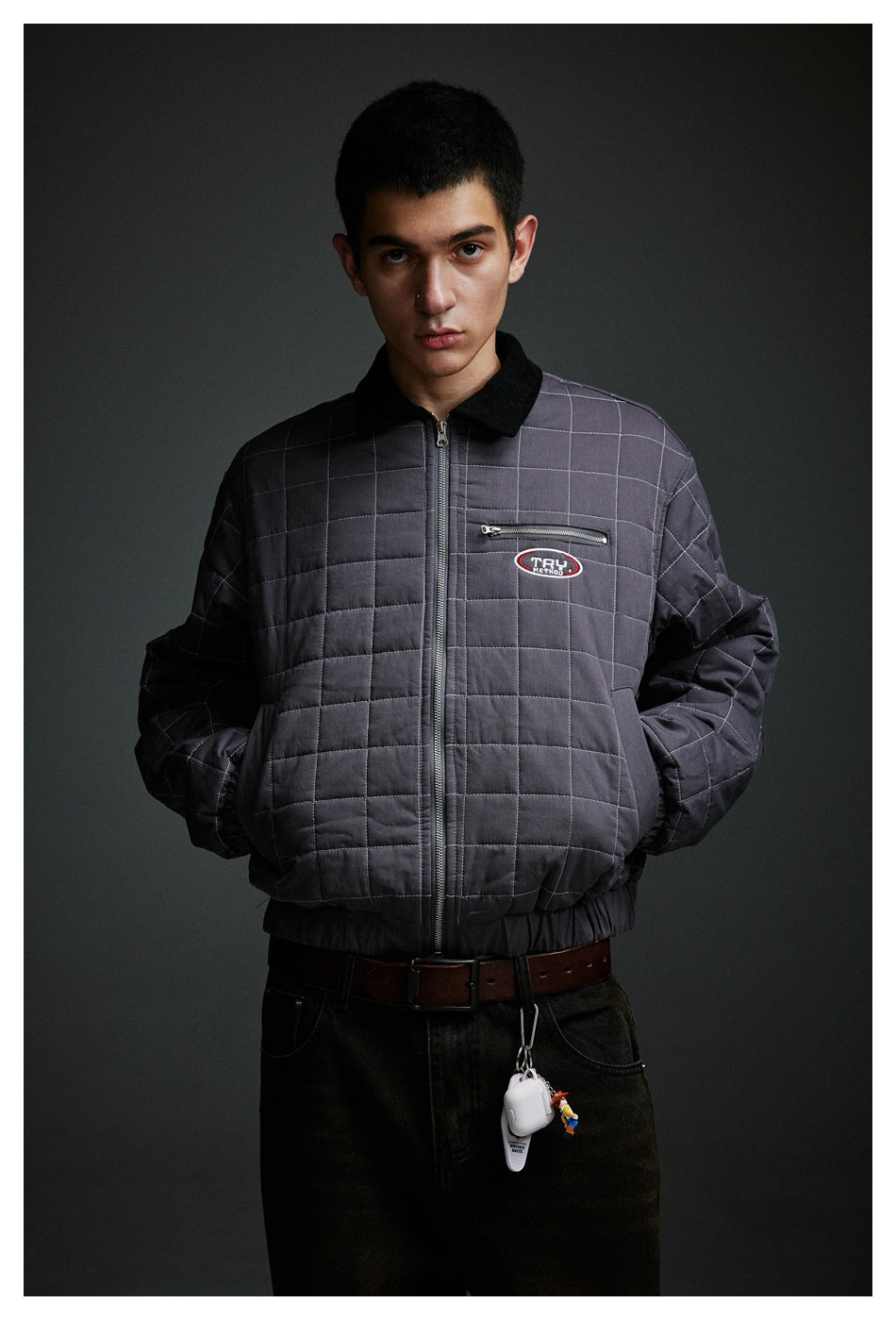 Close front view of a charcoal-gray quilted jacket on a model, showing its black collar, grid stitching, and chest zipper.
