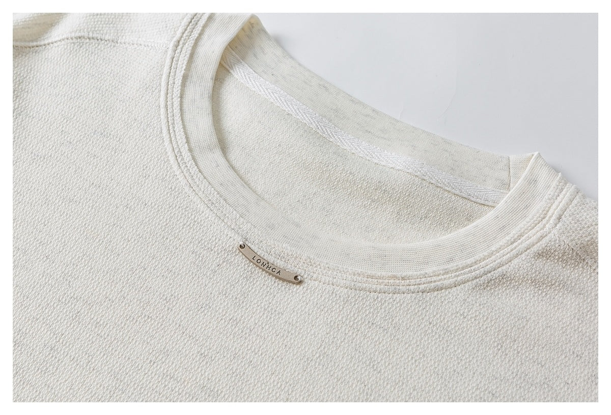 Close-up of an ivory textured top's ribbed crew neckline and small metal LONHCA plaque.