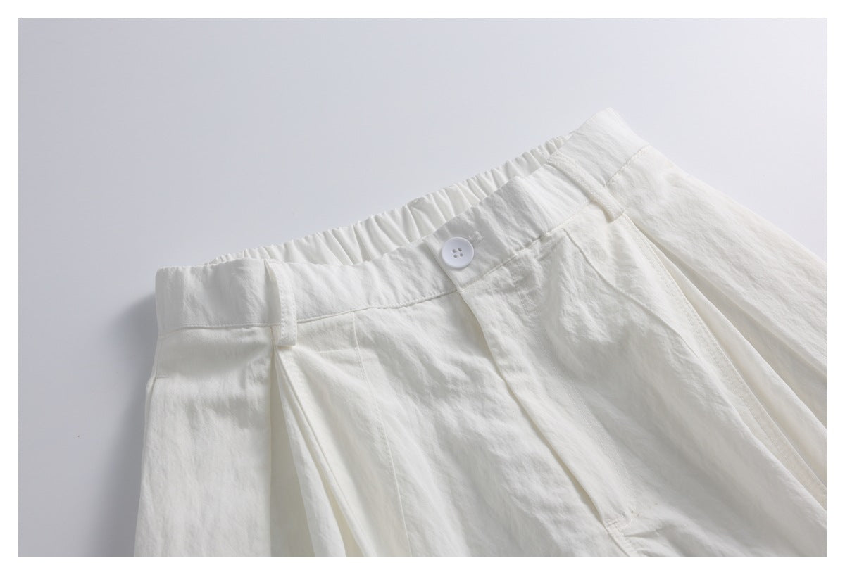 Close-up of off-white trousers with a gathered waistband, belt loop, white button and front pleats.