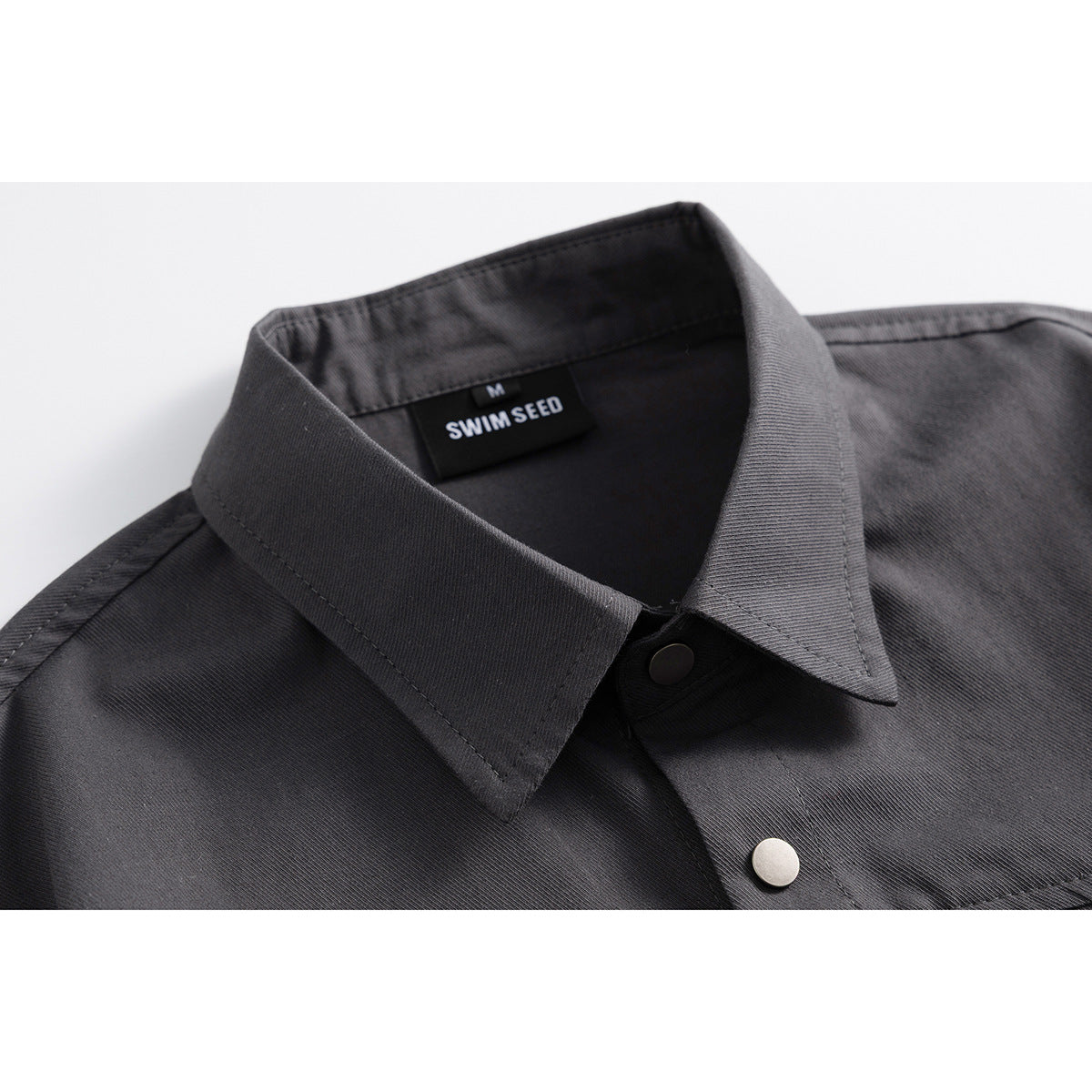 Close-up of a charcoal short-sleeve shirt collar, neck label, and metal snap buttons.
