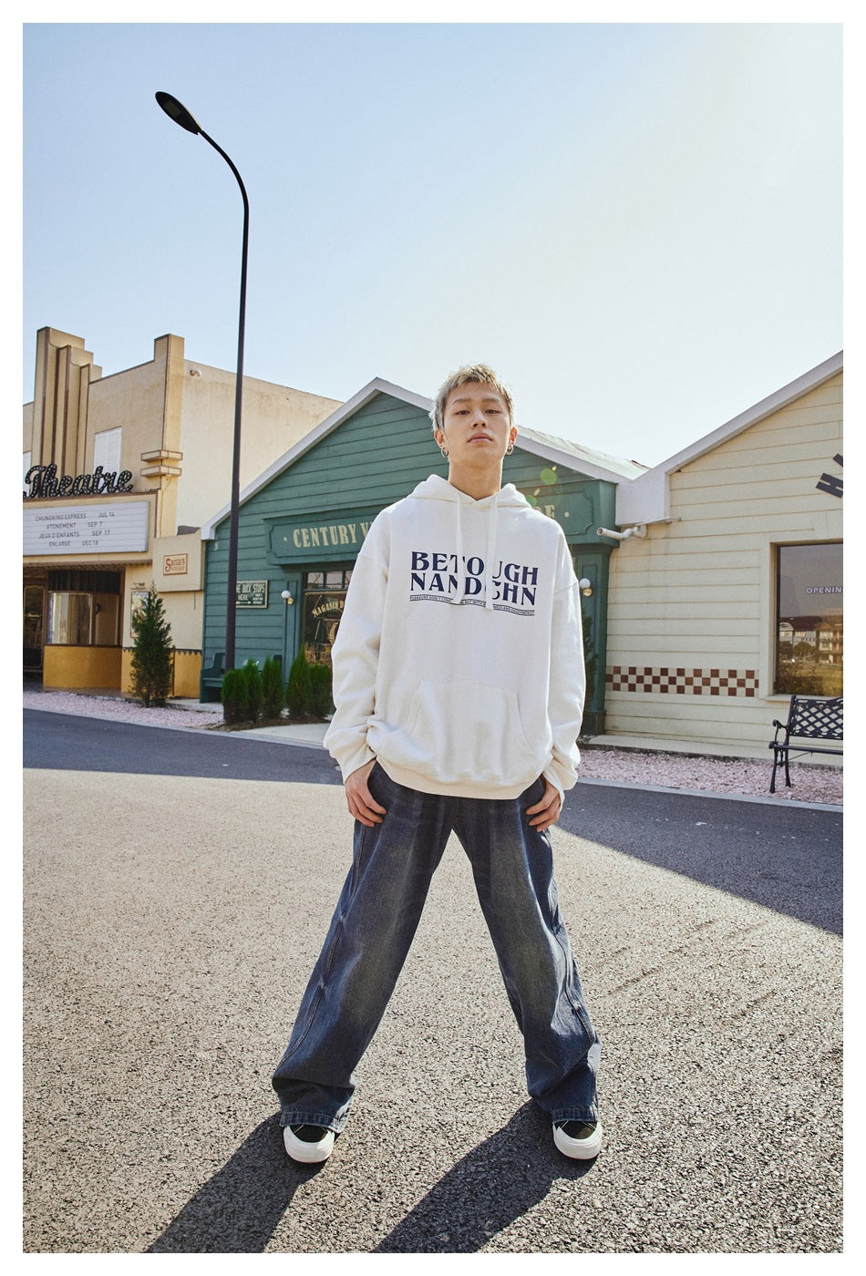 Front view of a model wearing a white graphic pullover hoodie with drawstrings and a kangaroo pocket, paired with wide-leg