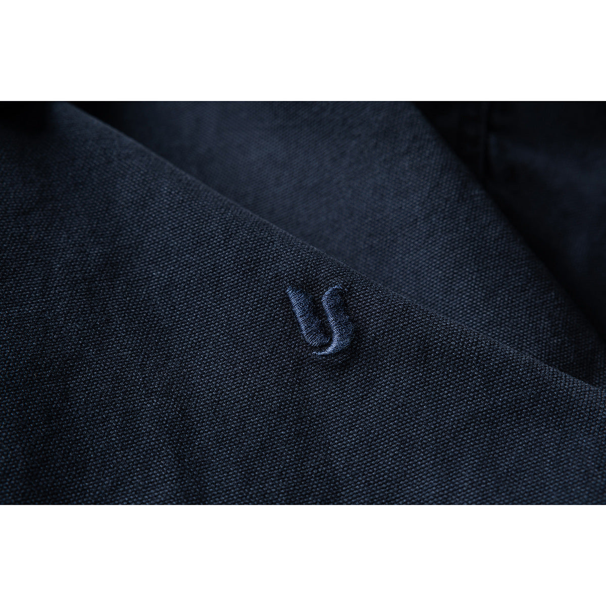 Close-up of a small dark embroidered emblem on textured navy jacket fabric.
