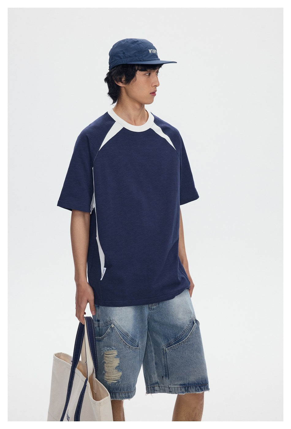 Model wearing a navy raglan T-shirt with white collar and shoulder panels, paired with distressed denim shorts.