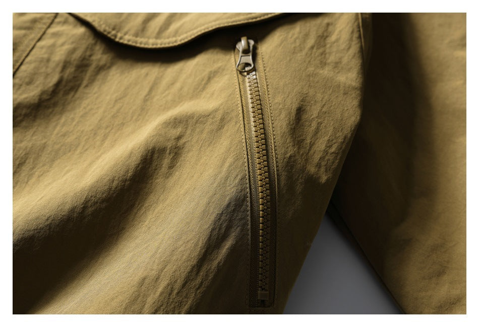 Close-up of a vertical zipper pocket on a tan olive jacket beneath a curved flap.