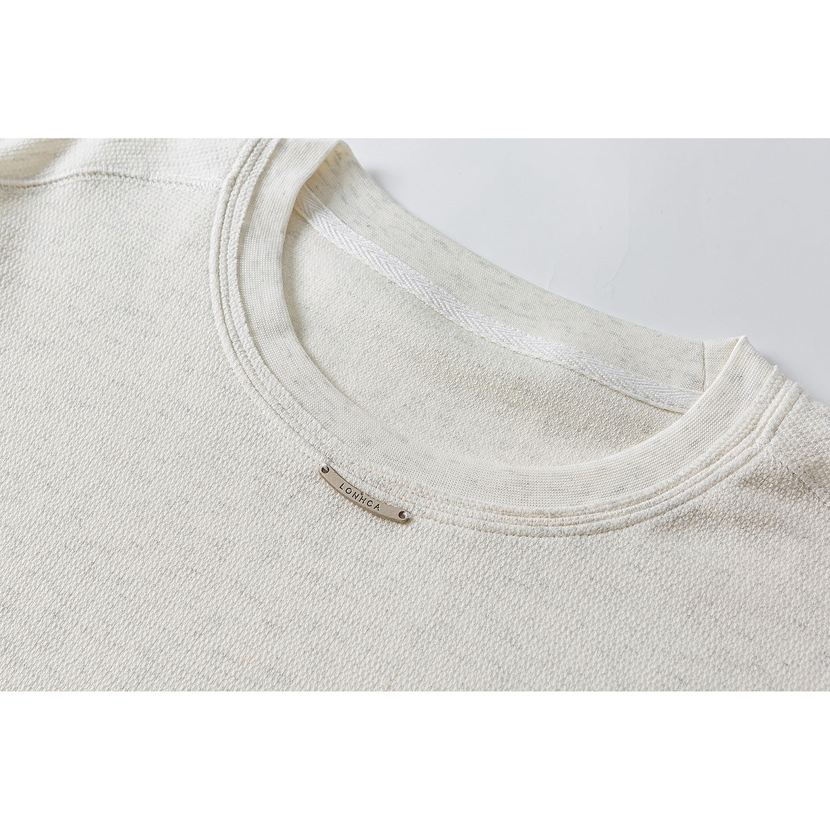 Close-up of an off-white textured long-sleeve shirt's crew neck and small metal collar plaque.