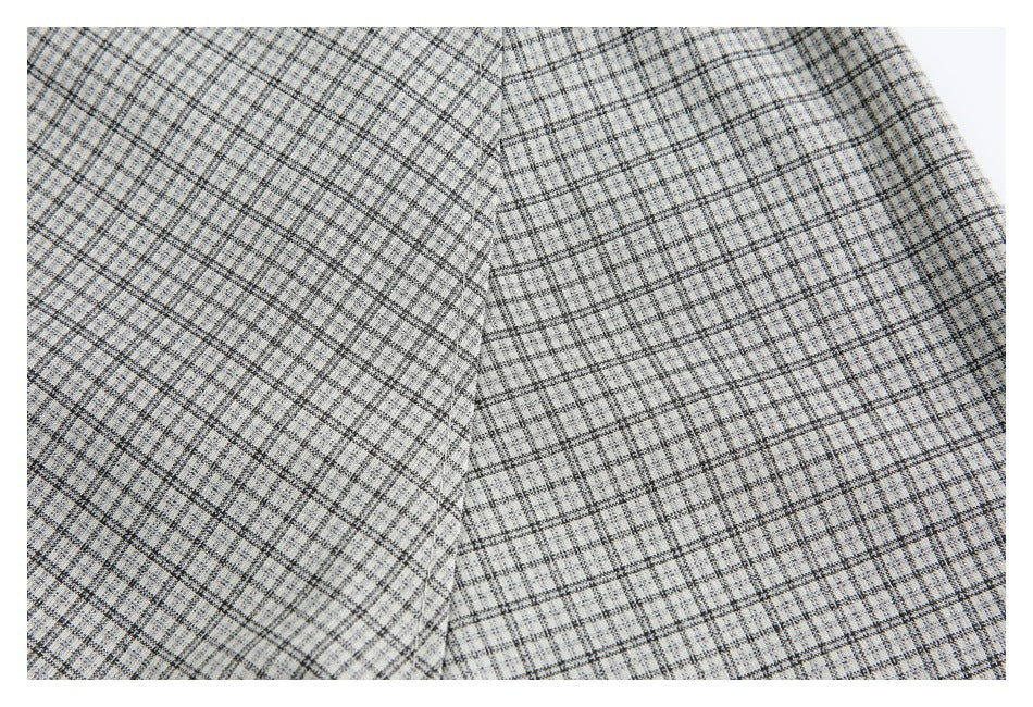 Close-up of light gray fabric with a fine black plaid pattern and a vertical seam.