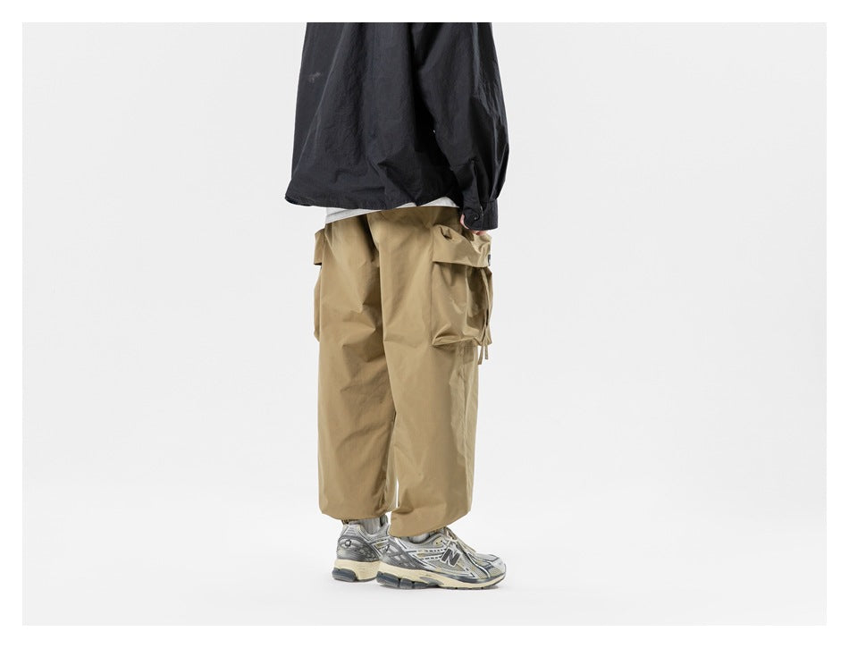 Rear view of a model wearing loose tan cargo pants with large side pockets and gathered cuffs.