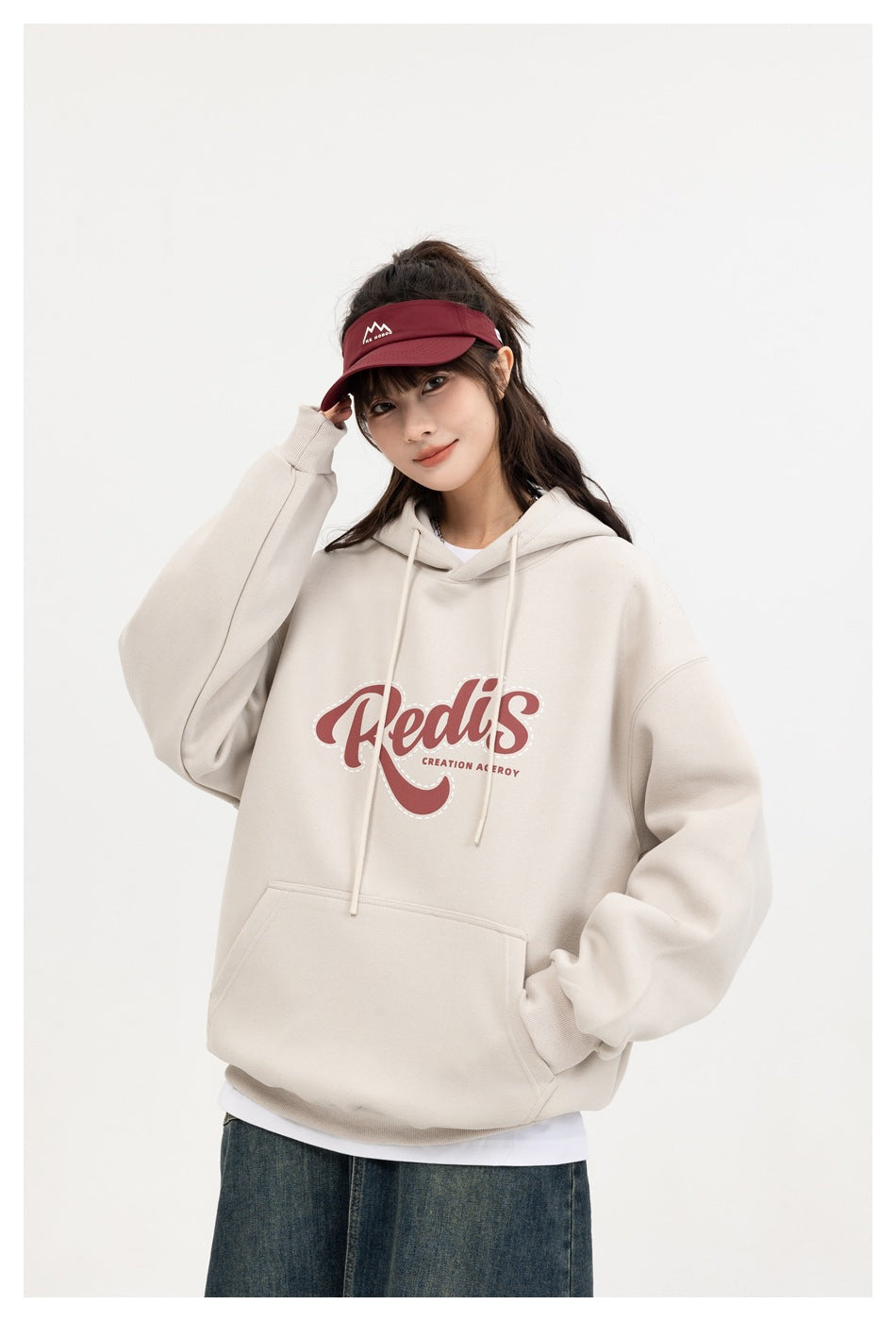Model wearing a cream pullover hoodie with drawstrings, a kangaroo pocket, and a red chest graphic.