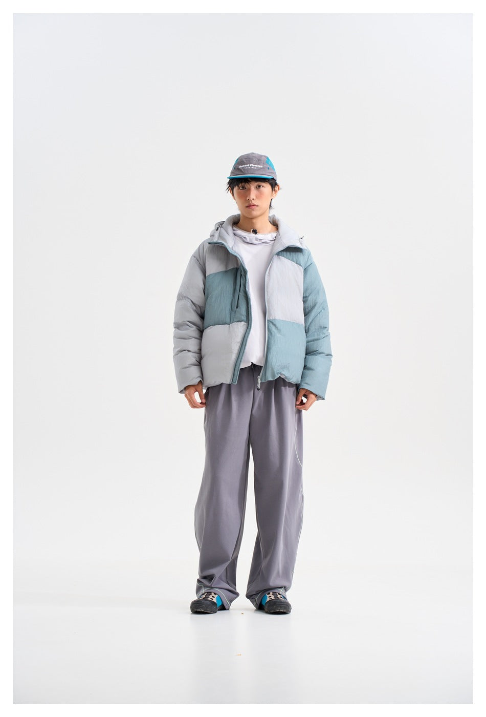 Front view of a model wearing a color-block puffer jacket in pale blue, gray, and white, with a hood and front zipper.
