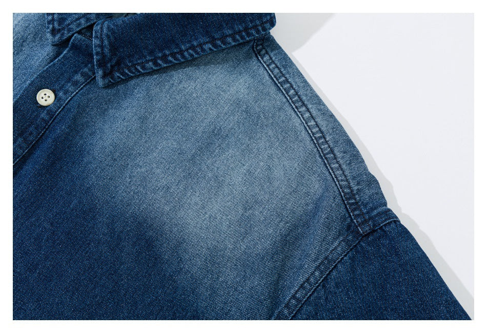 Close-up of a faded shoulder panel, collar edge, and stitching on a blue denim shirt.