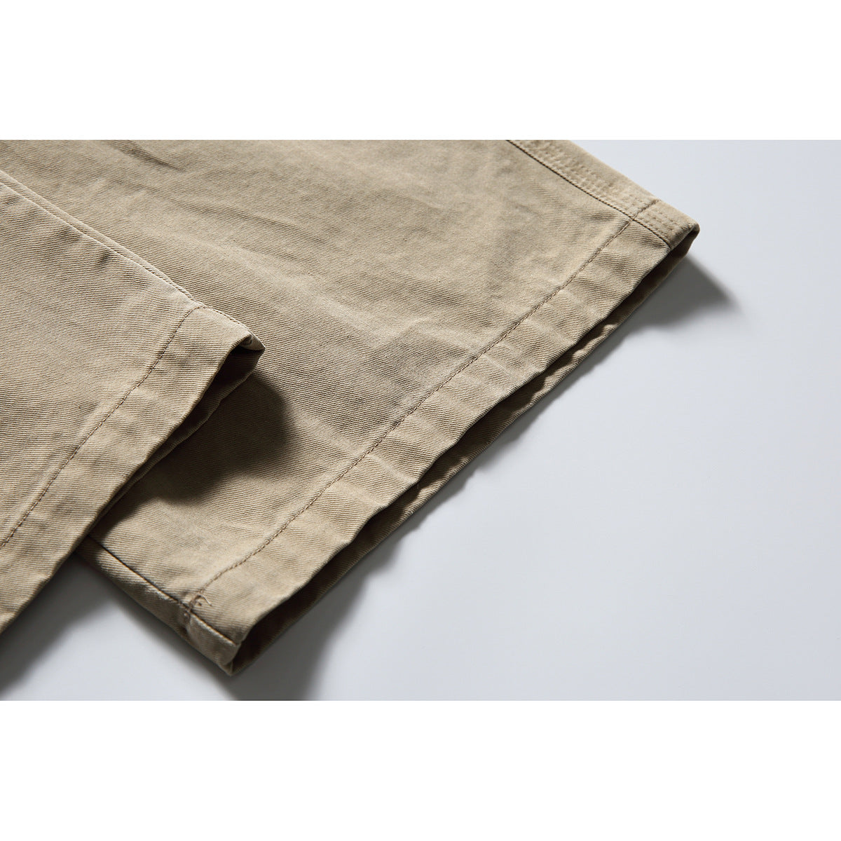 Close-up of the stitched hem and folded leg of tan trousers.