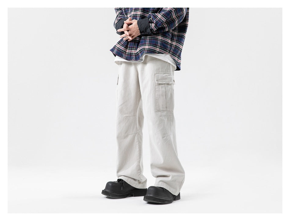 Front view of a model wearing loose light gray cargo pants with a flap thigh pocket and black shoes.