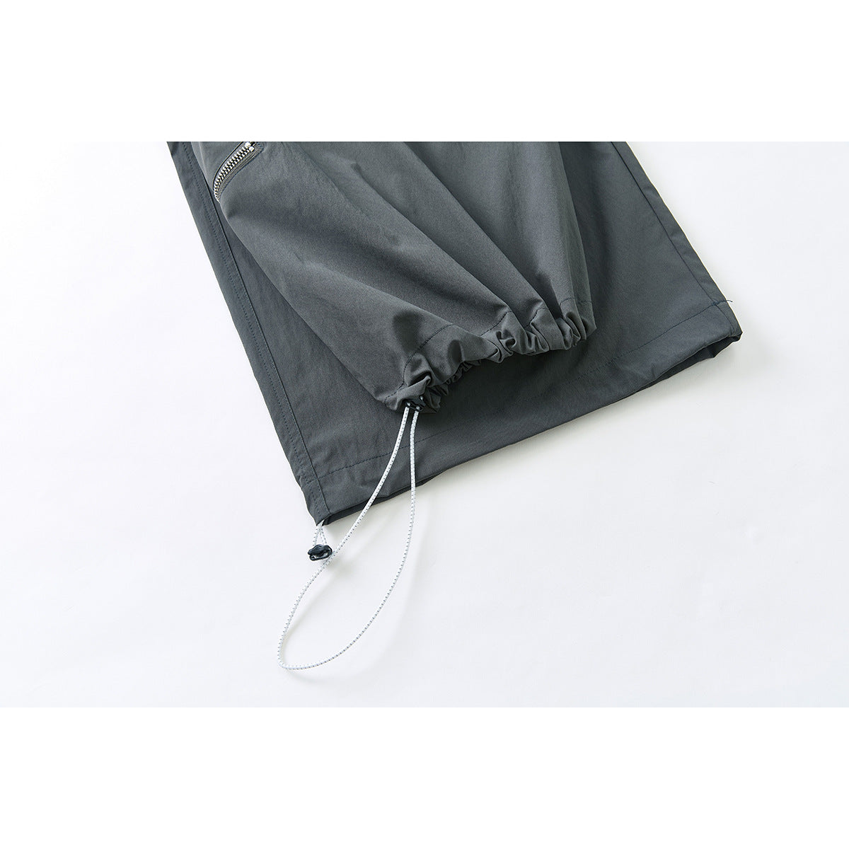 Close-up of dark charcoal pants showing a gathered ankle cuff with an adjustable drawcord.