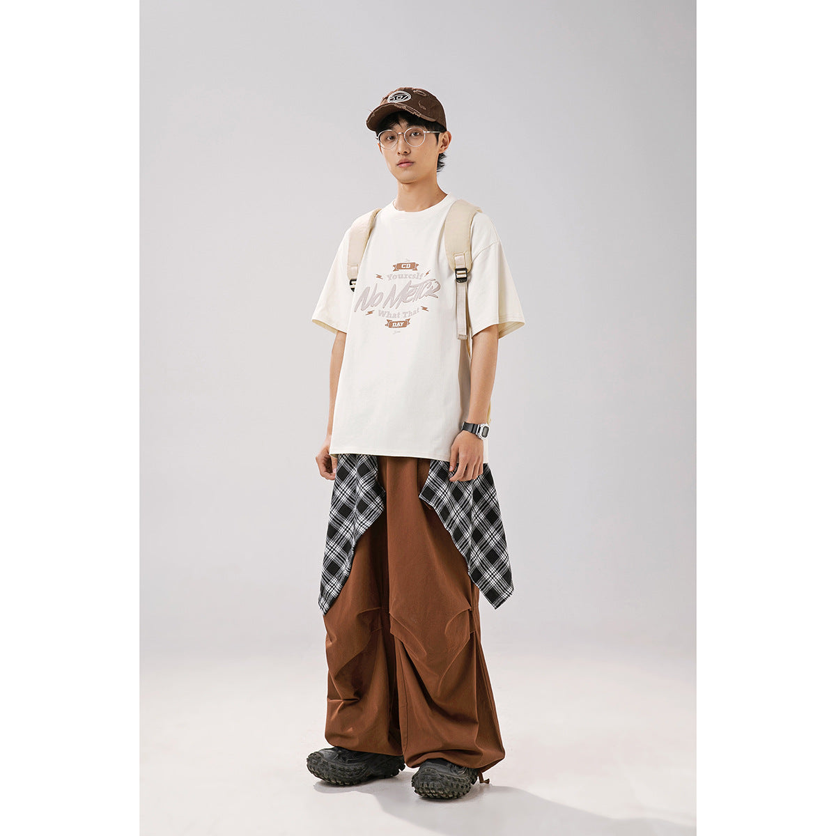 Model wearing an off-white graphic T-shirt with brown wide-leg pants and a plaid shirt tied around the waist.