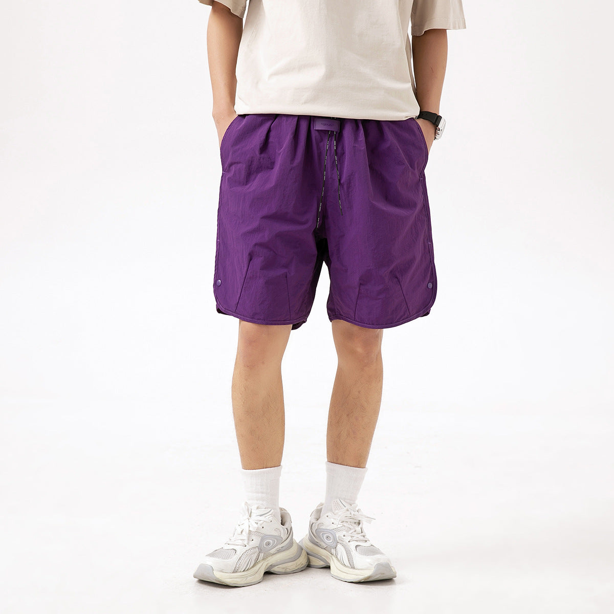 Model wearing loose purple shorts with a drawstring waist and side snaps, shown from the front.