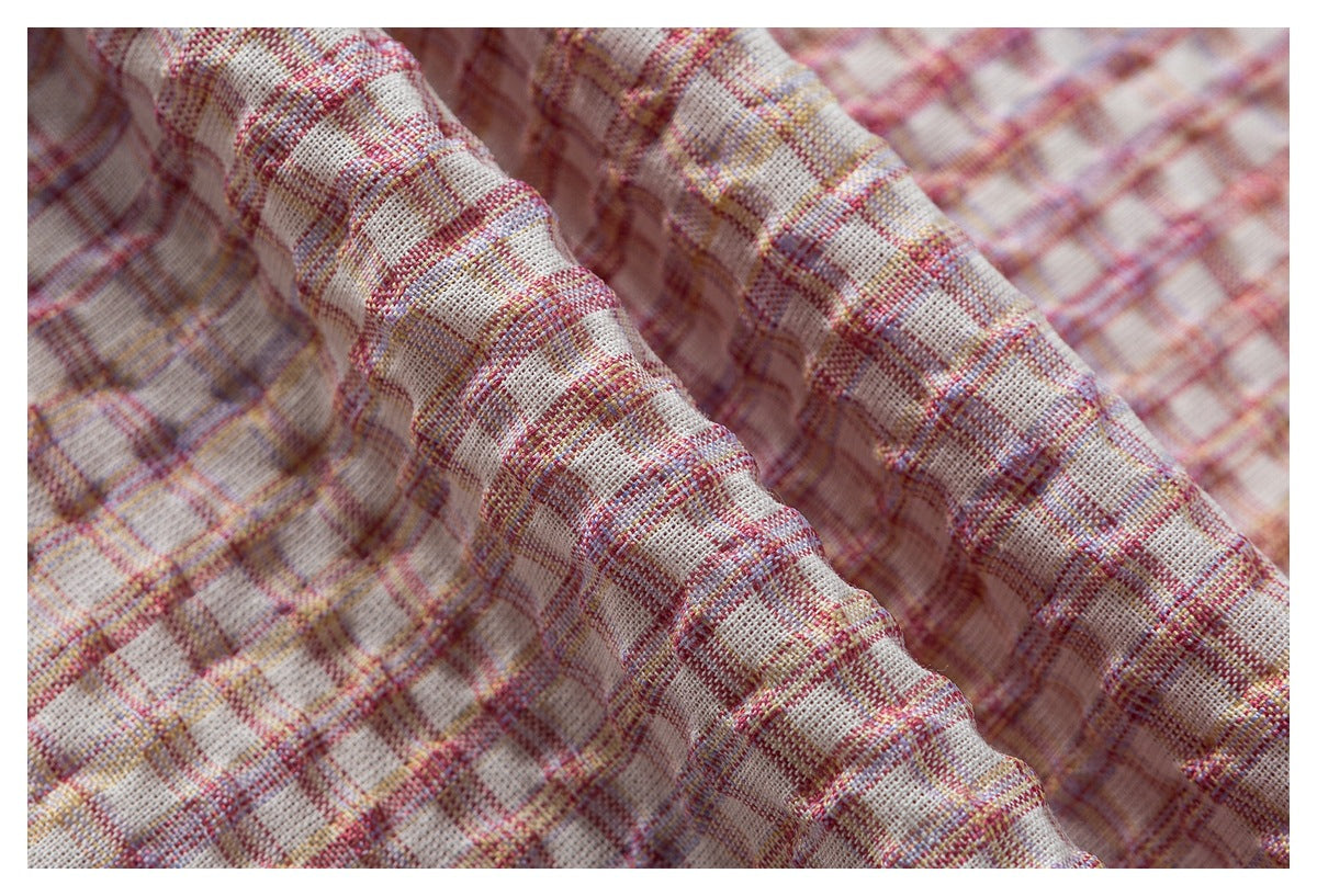 Close-up of textured cream fabric with a pink, mauve, and yellow plaid pattern.