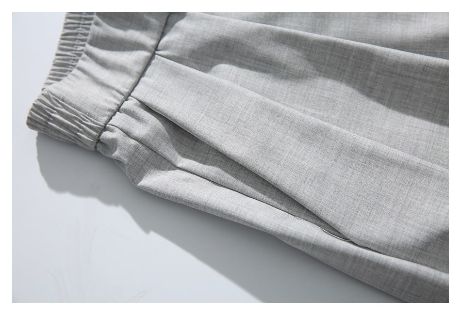 Close-up of the gathered elastic waistband and pleated side area of light gray trousers.