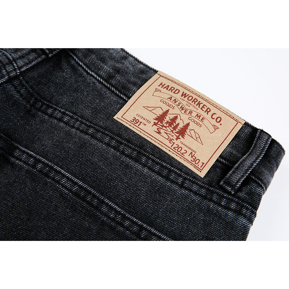 Close-up of black denim jeans with a tan leather-style waistband patch bearing English lettering.