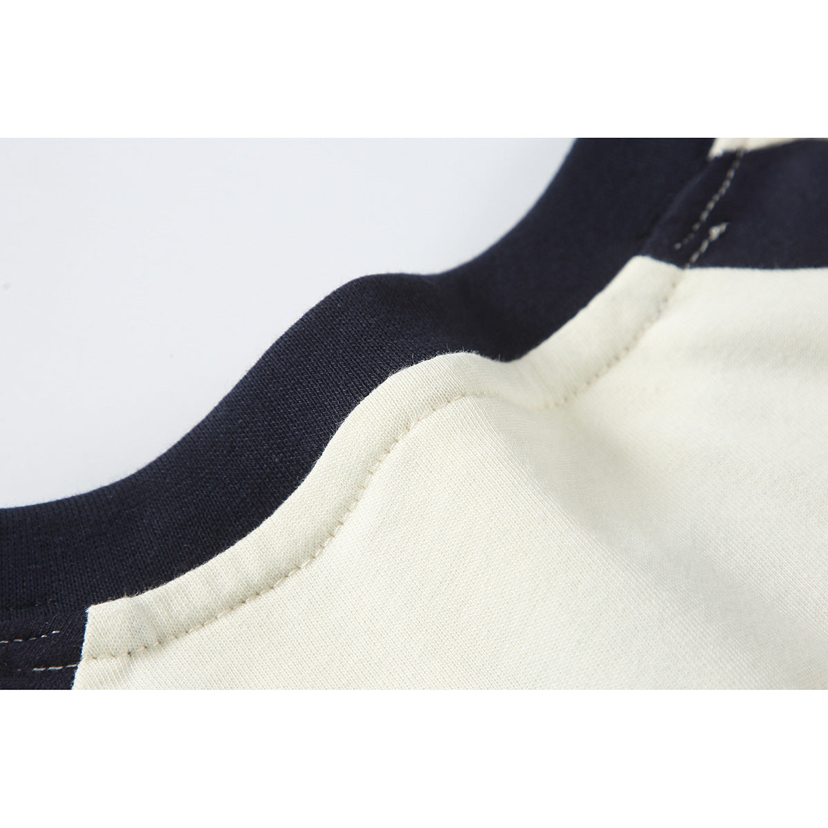 Close-up of cream and navy T-shirt fabric at a curved seam, showing stitching and the contrasting neckline.