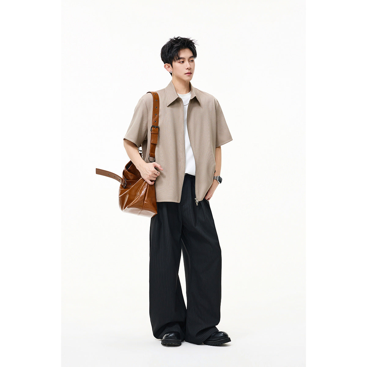 Model wearing a taupe short-sleeve collared zip-front shirt over a white tee with wide black trousers.