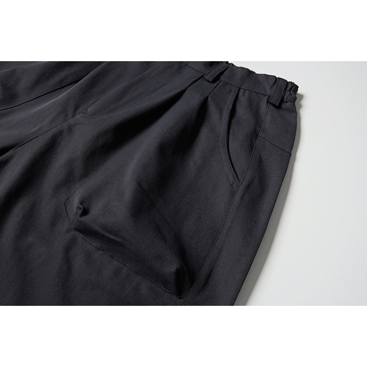 Close-up of charcoal shorts showing a curved side pocket, waistband and belt loops.