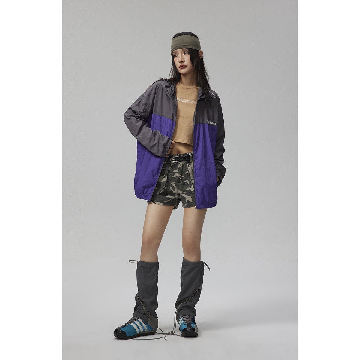 Model wearing a charcoal and purple hooded zip jacket with camouflage shorts and dark leg warmers.