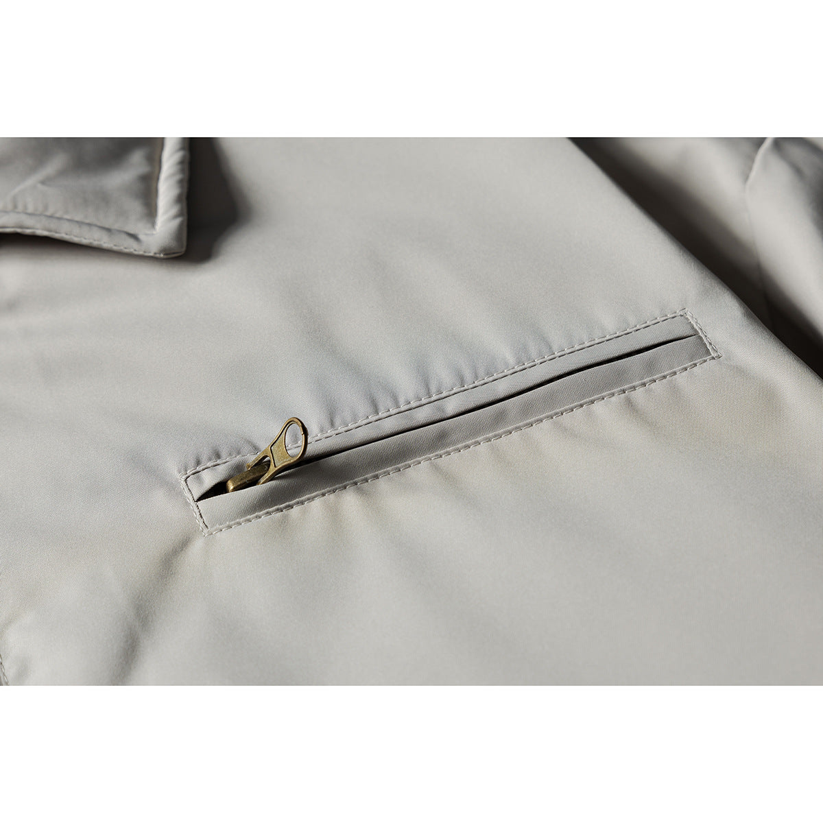 Close-up of a light gray jacket's slanted zip pocket with a brass-tone zipper pull.