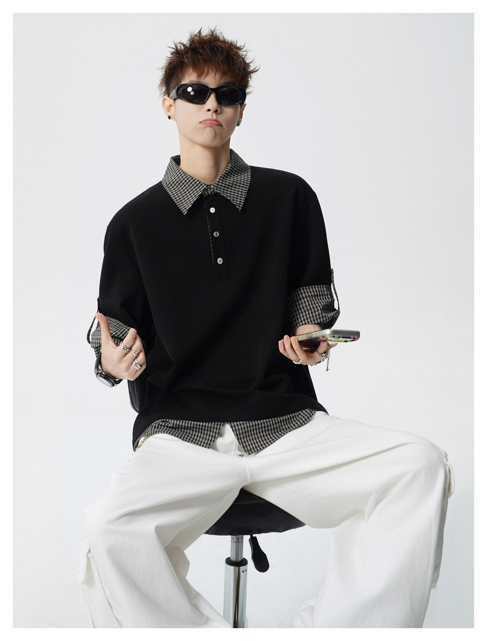 Seated model wearing a black polo with checked collar, cuffs and hem, paired with white trousers.